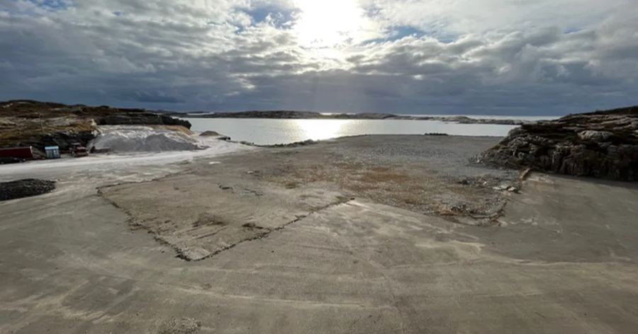 Levelled ground on the shoreline, with open sea beyond and low coastal rock on either side.